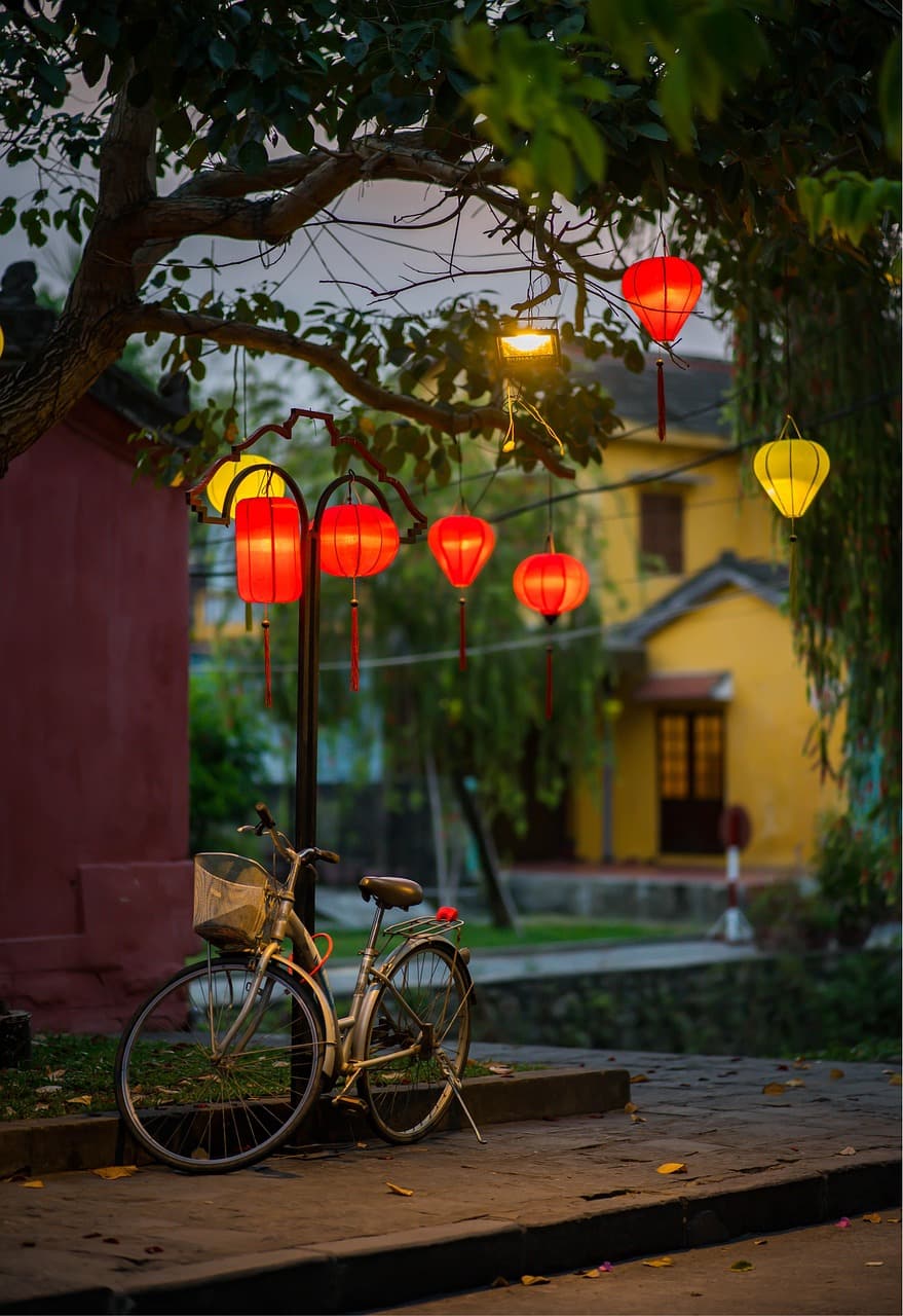 A row of multicolored silk lanterns glows above the Thu Bon River in Hoi An's Ancient Town with a small wooden boat carrying paper lanterns floating below